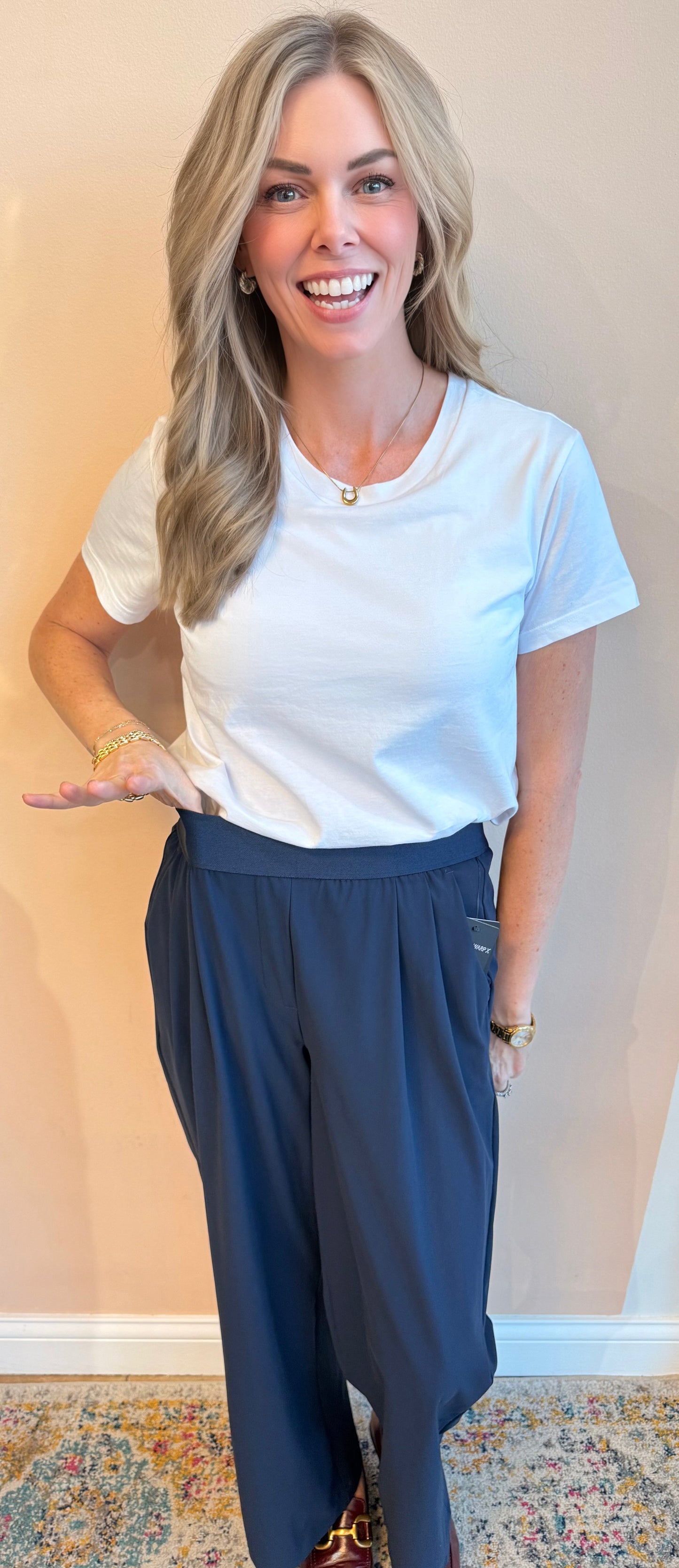 Woman wearing a white t-shirt and blue pants against a beige wall.