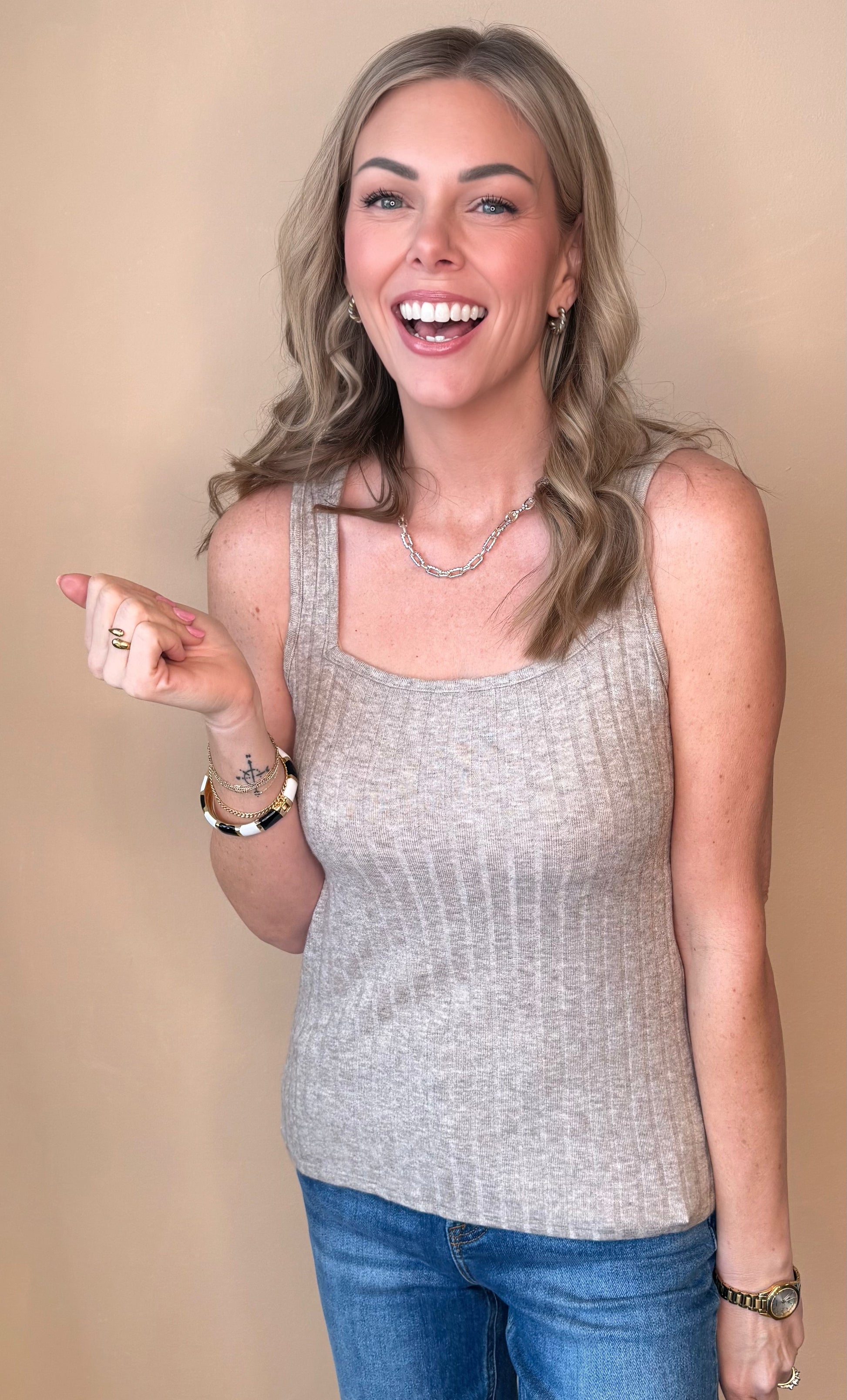 Woman wearing a gray sleeveless top and blue jeans against a beige background