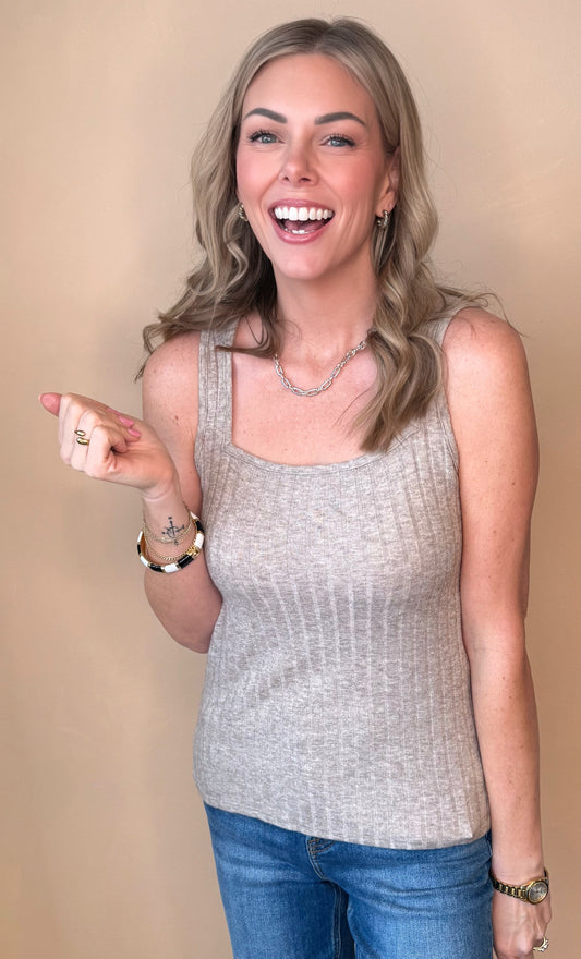 Woman wearing a gray sleeveless top and blue jeans against a beige background