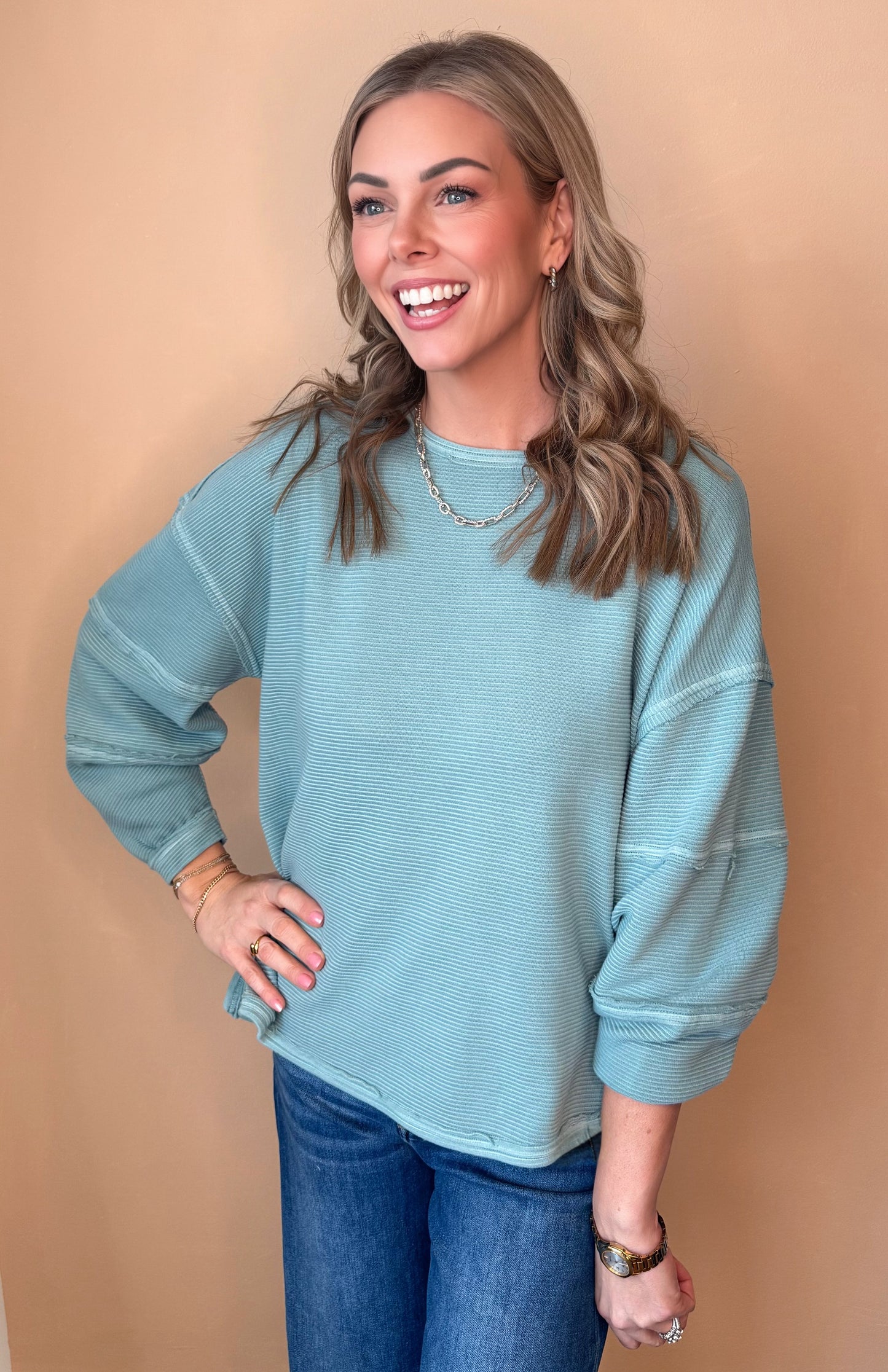 Woman wearing a teal sweater and blue jeans against a beige background