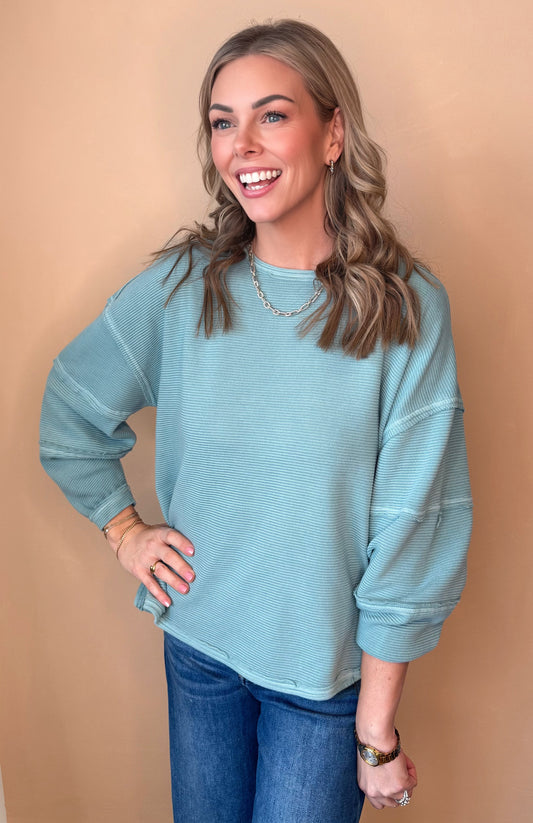 Woman wearing a teal sweater and blue jeans against a beige background