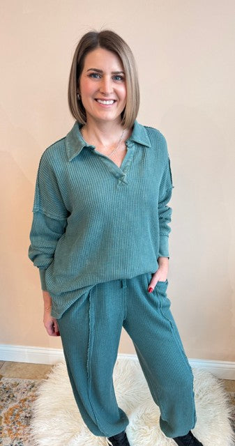 Woman wearing a teal outfit standing on a rug with a beige wall background